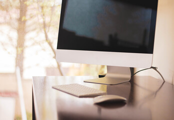 desktop computer on wooden table against light window with trees