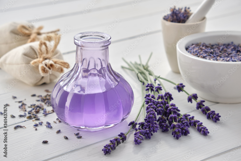 Dry lavender flowers, bottle of essential oil or flavored water, sachet and mortar on white wooden table. - obrazy, fototapety, plakaty 