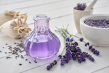 Dry lavender flowers, bottle of essential oil or flavored water, sachet and mortar on white wooden table.