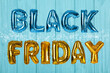 Phrase BLACK FRIDAY made of foil balloon letters on light blue wooden background