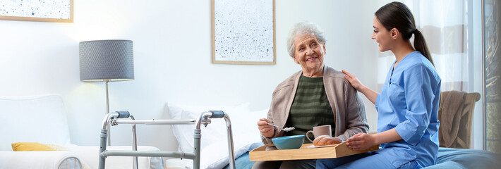 Canvas Print - Care worker serving dinner for elderly woman on geriatric hospice. Banner design