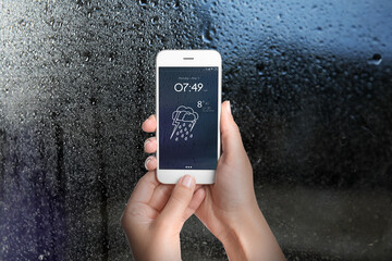 Wall Mural - woman using weather forecast app on smartphone near window indoors, closeup