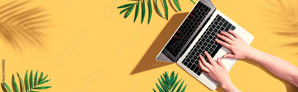 Person using a laptop computer with tropical leaves from above - obrazy, fototapety, plakaty 