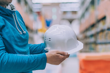 Wall Mural - A buyer in a hardware store selects a product. A man holds in his hand a white construction helmet for the head.