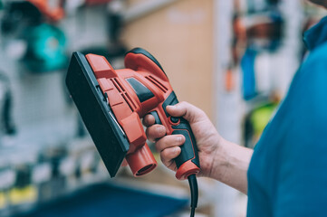 Wall Mural - A man holds in his hand a grinding machine on wood. A buyer in a hardware store selects a product.