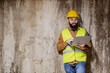 © Dusan Petkovic - Young bearded contractor leaning on concrete wall and checking on materials on laptop.
