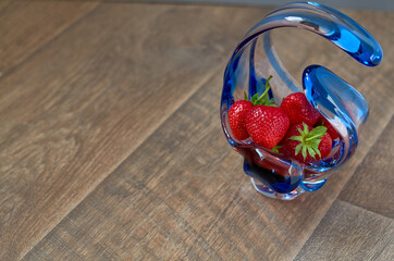 ripe red strawberries in a glass vase on a brown wooden background