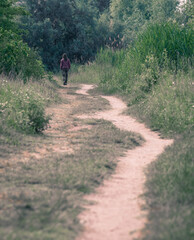 Lonely girl walking on a footpath surrounded by trees and high grass. Pathway in Vacaresti Park Nature Reserve.