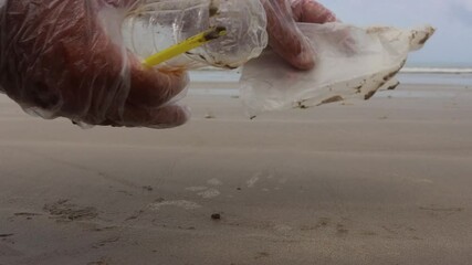 Poster - Picking up plastic trash from beach. Plastic bottles, bags, straws and cups litter a pristine beach. Environmental clean up