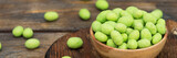 Fototapeta  - Fried peanuts in wasabi in a wooden bowl on a brown wooden table. Banner with space for text