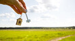 © Ольга Симонова - Wooden pendant of a house and key. Background of the sky and field. Dream of home, building a cottage in the countryside, plan and design, delivery of the project, moving to a new house. Copy space
