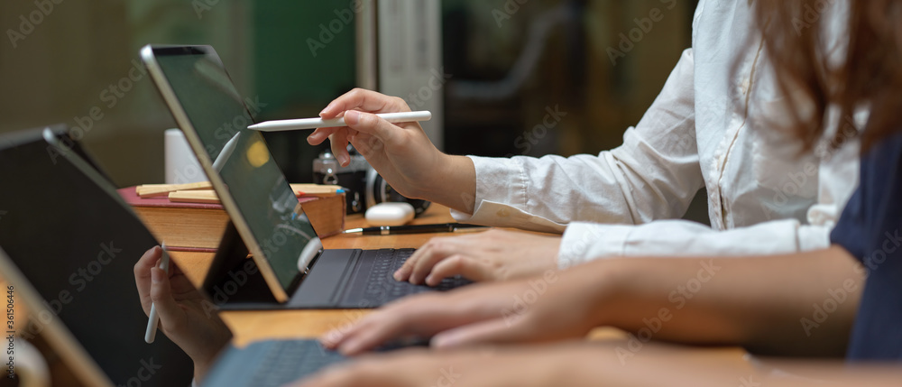 Two female workers consulting on their project while working with mock-up tablet on wooden table - obrazy, fototapety, plakaty 