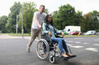 © H_Ko - Portrait of couple walking on city street. Charming woman sitting in wheelchair. Caring man accompany female friend. Walking on fresh air. Disabled people concept