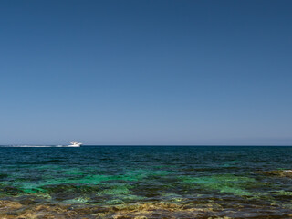 Speed boat on horizon of the Mediterranean sea seen from the shore on sunny day with clear skies