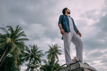 Lonely man on an old boat on a tropical island on a cloudy day