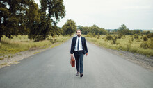 Businessman In Classic Suit Holding Briefcase Moving Forward In Middle Of Country Road Looking Camera