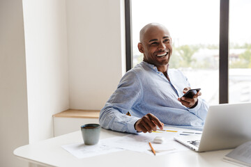 Wall Mural - Photo of african american man using cellphone while working with laptop