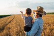 © cherryandbees - farmer holding his grandson standing in wheat field