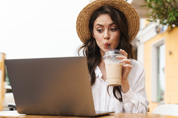 Poster - Portrait of young beautiful woman using laptop while drinking milkshake