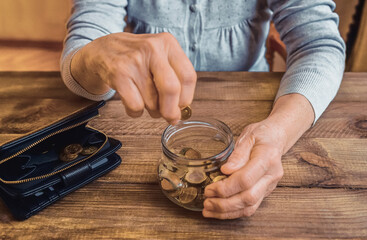 Wall Mural - Old wrinkled hand holding jar with coins, empty wallet, wooden background. Elderly woman throws a coin into a jar, counting. Saving money for future, retirement fund, pension, poorness, need concept.