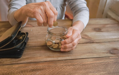 Wall Mural - Old wrinkled hand holding jar with coins, empty wallet, wooden background. Elderly woman throws a coin into a jar, counting. Saving money for future, retirement fund, pension, poorness, need concept.