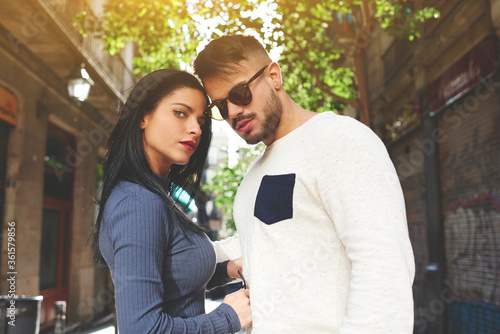 Stylish cute couple looking at the camera. Pretty brunette in a gray top pulled off her glasses to show her bright eyes.Her boyfriend in a white sweater with a black pocket decided to hide his glance