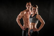 © Maksim Toome - Fitness in gym, sport and healthy lifestyle concept. Couple of athletic man and woman showing their trained bodies on black background. Two bodybuilder models standing and demonstrating tight muscles.
