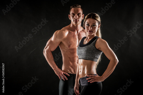 Fitness in gym, sport and healthy lifestyle concept. Couple of athletic man and woman showing their trained bodies on black background. Two bodybuilder models standing and demonstrating tight muscles.