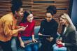 © BullRun - Cheerful multiracial women writing registration documents for training courses sitting together with modern technology, happy female students signing pepers of information agreement before workshop