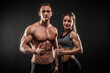 © Maksim Toome - Fitness in gym, sport and healthy lifestyle concept. Couple of athletic man and woman showing their trained bodies on black background. Two bodybuilder models standing and demonstrating tight muscles.