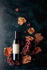 Poster - Bottle of red wine with ripe grapes and dried up vine leaves.