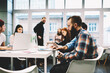 © BullRun - Young hipster male architect working with laptop computer while his colleagues discussing new successful startup project. Spanish student man searching information in internet to prepare for exams