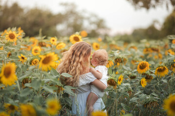 Young beautiful mother holds on hands a little curly daughter. Motherhood. Curly mom and little daughter in a sunflower field. Summer.