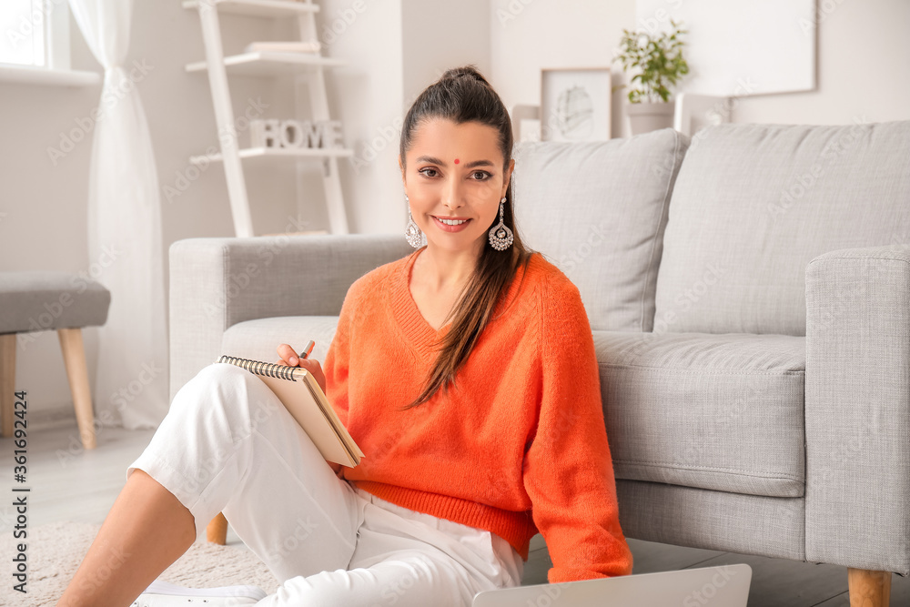 Beautiful young woman with laptop and notebook at home