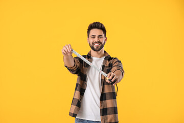 Young man with measuring tape on color background