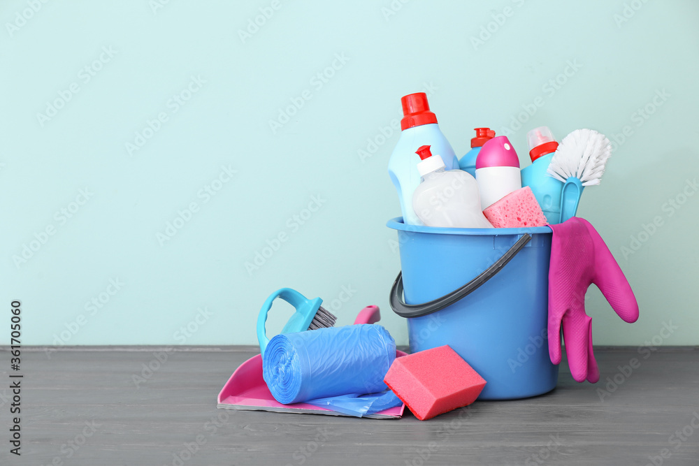 Bucket with set of cleaning supplies on table