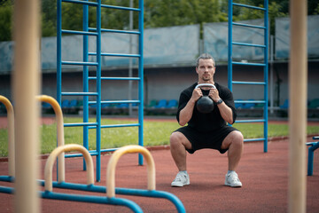 Wall Mural - young athlete has workout and doing sport exercises with kettlebell outdoor