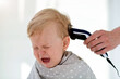 © smile35 - Female hands trim a crying baby with an electric hair clipper in a hairdresser. First haircut.