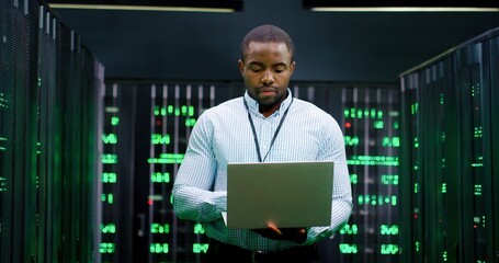 male system administrator of big data center typing on laptop computer while working in server room.