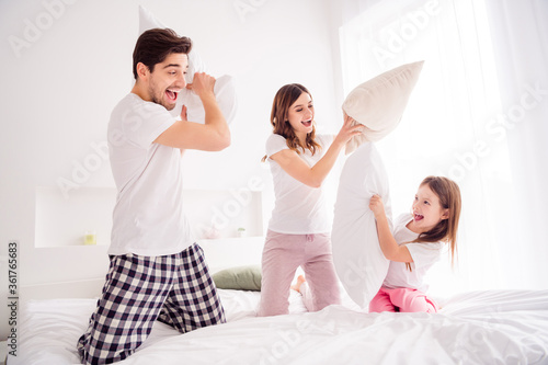 Photo of young family mommy daddy daughter sheets good mood spend together quarantine weekend playing games pillow fighting self isolation offspring bed bedroom indoors