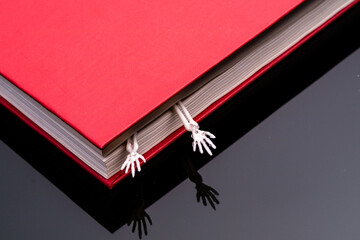 two hands of a human skeleton stick out from a closed red book. scary secrets secrets books