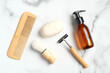 Flat lay composition with bath accessories and shaving tools for man on marble background. Top view wooden hair comb, handmade soap, shaving brush, razor, shampoo bottle.