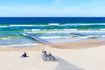 Wall Mural - Woman tourist sitting on beautiful white sand beach near Kolobrzeg, Baltic Sea coast, Poland