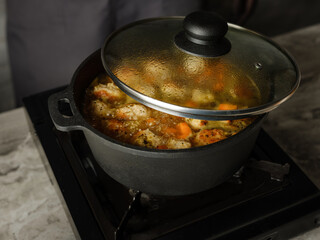 Cooking soup with meatballs cutlets and vegetables in big pan pot on home kitchen background by chef hands. Copy space, closeup. Homemade food recipe concept.