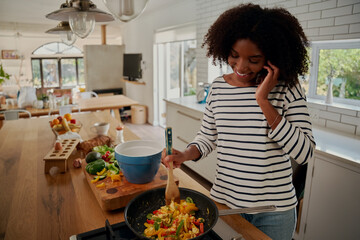 Happy african young woman talking on smartphone while preparing meal during covid-19 lockdown