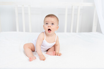 Wall Mural - Baby boy 8 months old sitting in a crib in a children's room in white clothes and looking away, baby's morning, baby products concept