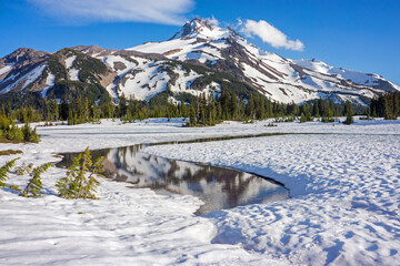 Wall Mural - volcanic mountain peak under a crisp blue sky rises behind a field of snow. calm water in the foregr
