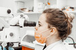 © Natalya Lys - Young woman dentist at her workplace. The doctor uses disposable gloves, a mask and a hat. The dentist works in the patient's mouth, uses a professional tool.