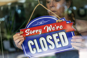 Wall Mural - Sad Female Store Owner Turning Sign to Closed in Window