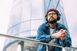 © mykolastock - Thoughtful young bearded man dressed in denim shirt looks away enjoys mysic in headphones in the city